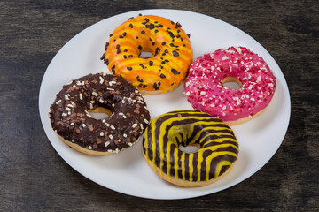 Doughnuts with different glazes, sprinkles, on dish on black surface