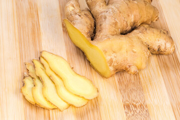 Partly sliced fresh ginger root on cutting board close-up