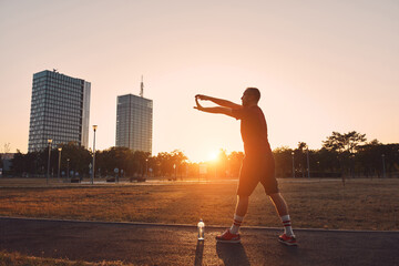Sporty man stretching in an urban park during sunset time.