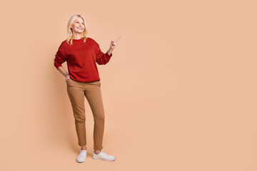 Full length photo of positive dreamy lady dressed red pullover looking showing finger empty space isolated beige color background