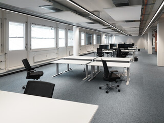 Empty office space with desks and chairs, large room, natural window light, no people