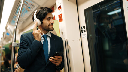 Smart executive manager wear headphone and listen music while standing in train. Professional business man lean at partition while listen relaxed song and choosing songs. Business concept. Exultant.