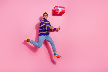 Full body photo of attractive young man jumping thumb up giftbox dressed stylish violet striped...
