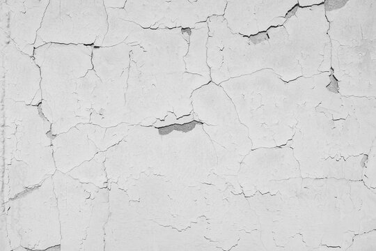Peeling  white paint on the concrete wall with old cracked flaking paint. Weathered rough painted surface with patterns of cracks and peeling. \ texture for background