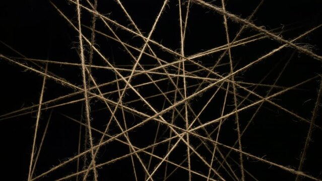 Macro dolly shot camera flies through sisal ropes, threads plexus lighted with spot light on black background, twine lines in dark, abstract chaotic interweaving, background for titles or logo