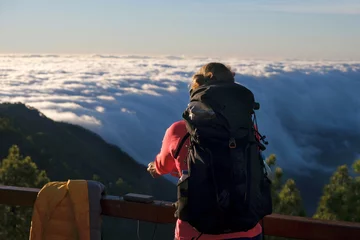 Foto op Canvas Woman with backpack is looking to mountain panorama with sea of clouds in sunrise scenery. Refugio Punta de Los Roques,  National Park Caldera de Taburiente. La Palma, Canary Islands, Spain © Iwona