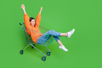 Full length photo of delighted funky girl sit inside market trolley raise fists empty space...