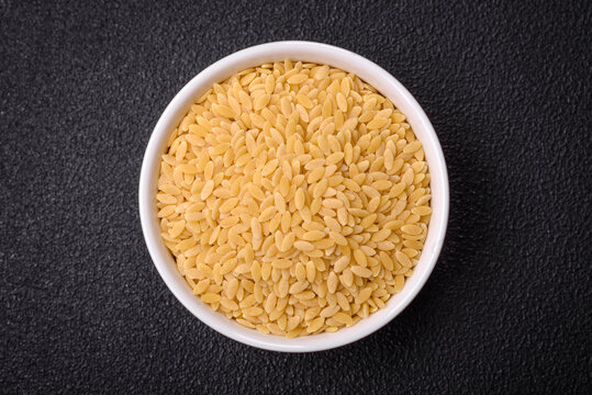Raw risoni pasta made from durum wheat on a dark concrete background