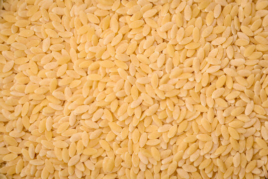 Raw risoni pasta made from durum wheat on a dark concrete background
