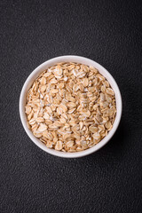 Raw oatmeal flakes in a ceramic bowl on a dark concrete background