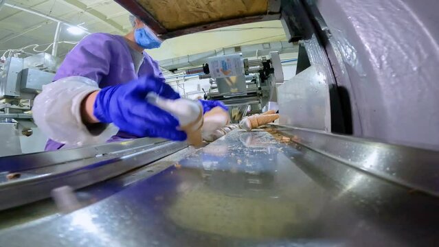 The worker lays out the ice cream on the conveyor with his hands in the right order. A worker on a conveyor lays out ice cream. Production of ice cream at the factory.