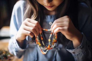 Deurstickers girl adjusting a beaded necklace, accessory detail in the forefront © studioworkstock