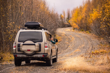 A woman sitinng in a SUV on а scenic autumn road in the forest and smiling - obrazy, fototapety, plakaty