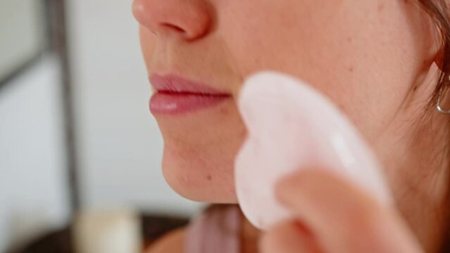 Close-up of a young woman doing a facial massage with a Gua Sha stone scraper.