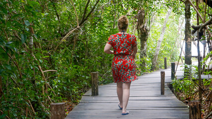 woman from behind walking on wooden walkway in the middle of the jungle
