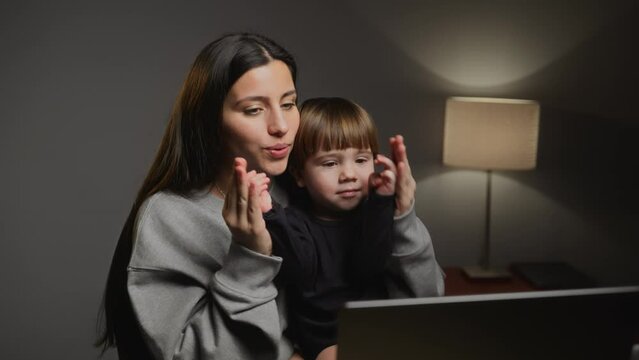 A mom with a baby watching cartoons. A young mom with a small child sits in front of a laptop. Mom and son dancing and laughing. Mom kisses her son. Family. Laptop. Watching a movie. Entertainment