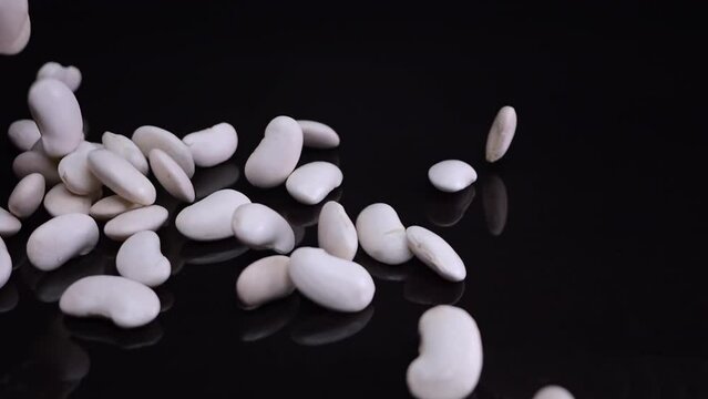 Slow-motion footage of white beans falling onto a shiny black base, spilling from glass jars, a vegan culinary staple.