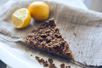 Side view of a piece of healthy, organic, gluten-free, sugar-free, dairy-free dessert with lemons with copy space. Homemade organic dessert with two lemons on the grey fabric. Selective focus 
