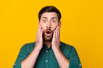 Photo of speechless man with brunet hair dressed dotted shirt staring palms on cheekbones isolated on vibrant yellow color background