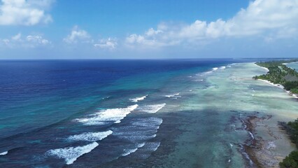 Drone view of paradise islands of the Maldives with coral reefs under the waves of blue the Indian Ocean.