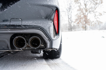 Double pipe exhaust system with carbon fairing on a black new sports car in winter while it is snowing