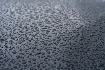 Close-up of sleet, drops on a black hood, on a black new car 