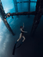 Woman free diver swims underwater on deep in transparent ocean. Freediving under the pier