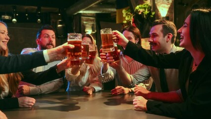 Cheers. Co-workers, employees meeting after work at pub, drinking foamy lager beer, talking, having fun. Concept of leisure time, friendship, fun and joy, youth, enjoyment