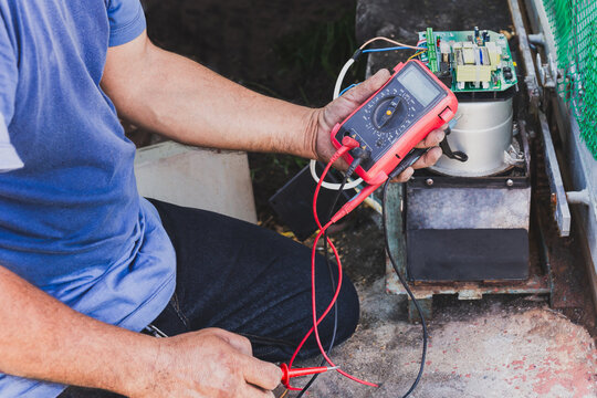 Electrician checking mainboard with multimeter outdoors at home.