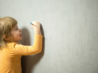 cute little girl draws with a colored pencil on the wall. Children's work,little girl draws with a felt-tip pen on the wallpaper at home