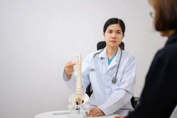 An orthopedic surgeon or therapist is showing a spinal model and explaining to a female patient her spinal problems. Health care concept and aging and back pain