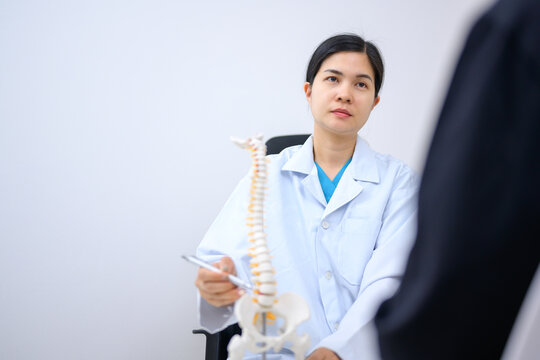 An orthopedic surgeon or therapist is showing a spinal model and explaining to a female patient her spinal problems. Back pain and health care concept