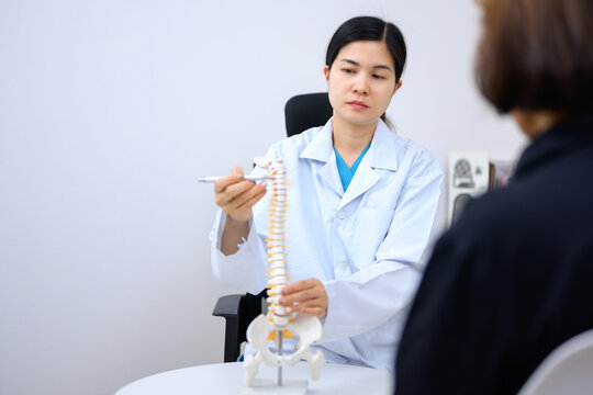 Asian female doctor points to spine model and explains female patient about her spine problem Health care concept and aging and back pain