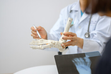An orthopedic doctor points to a model of ankle and foot bones explaining to a patient a foot bone...