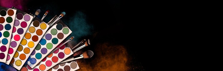 Bright eye shadow, blush brushes, explosion of multicolored powder dust on black background. Highly vibrant color-pressed pigment palettes for make-up. Abstract background for cosmetic concept.