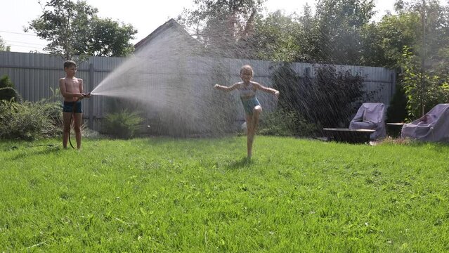 Summer holiday. Happy two kids siblings playing with garden hose and having fun with spray of water in sunny backyard. Summer time. 