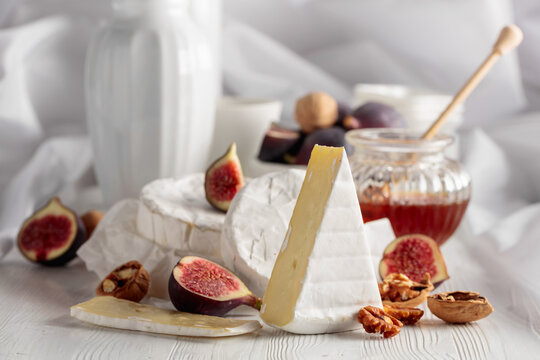 Camembert cheese with figs, walnuts, and honey on a white table.
