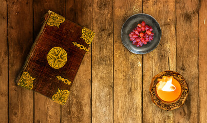 An old book with decorative cover with candle and grapes on an old table from planks