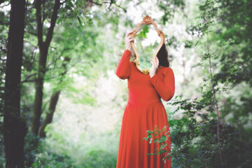 woman in red dress covers her face with a mirror that reflects the surrounding forest - 726455579