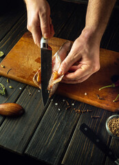 The chef cuts fresh Merluccius fish with a knife on a wooden cutting board. Home-cooked national...