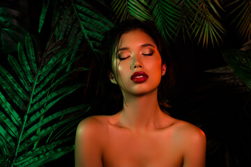 Photo of vietnamese japanese girl over dark green palm leaves closing eyes with decorative makeup