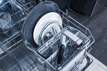 Dishwasher with dirty plates, knives and pot lid. Washing dishes