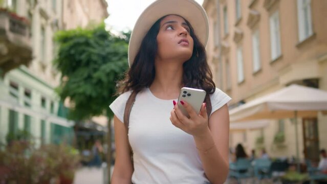 Upset Indian Hispanic ethnic woman female tourist traveler lady lost on city street abroad looking around searching use cellphone GPS app online find explore town smartphone problem confusion outside