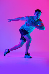 Fototapeta na wymiar Athletic man in comfortable sportswear, with muscular body training against gradient pink background in neon light. Concept of active and healthy lifestyle, sport, fitness, endurance