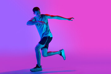 Fototapeta na wymiar Warming-up exercises. Sportive young man in sportswear training, doing exercises against gradient pink background in neon light. Concept of active and healthy lifestyle, sport, fitness, endurance