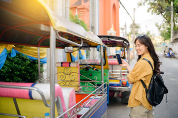 Young Asian woman backpack traveler standing a side of Tuk Tuk taxi on summer vacations at Bangkok, Thailand. Journey trip lifestyle, Asia summer tourism concept. - obrazy, fototapety, plakaty