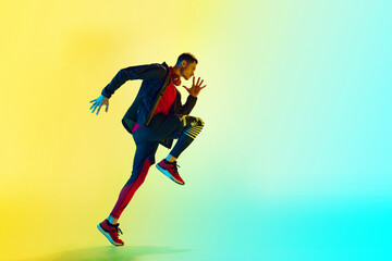 Dynamic image of young athletic man in sportswear, training, running against gradient blue yellow background in neon light. Concept of active and healthy lifestyle, sport, fitness, endurance