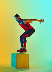 Fototapeta na wymiar Full-length dynamic image of y9ung muscular man training, jumping on block, training against gradient blue yellow background in neon light. Concept of active and healthy lifestyle, sport, fitness