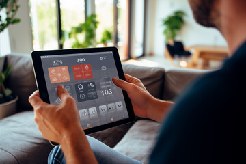 A person is using a tablet with smart home app in modern living room  Adjusting a temperature - obrazy, fototapety, plakaty