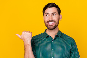 Fototapeta premium Photo of satisfied man with brunet hair dressed dotted shirt look directing at offer empty space isolated on yellow color background